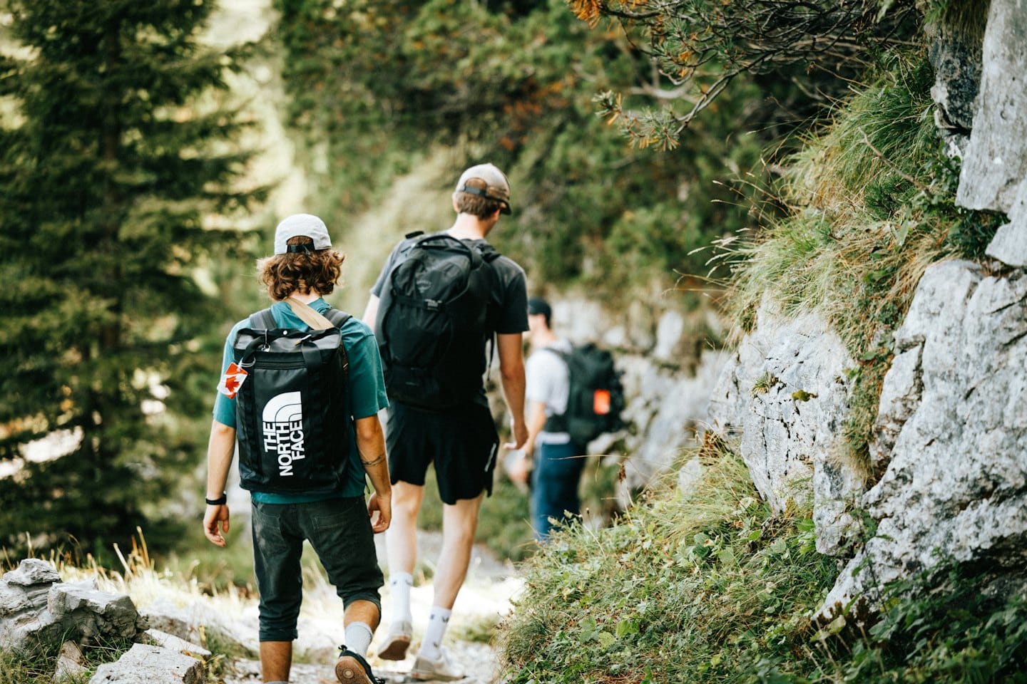 Tres personas caminan por un sendero de montaña rodeado de árboles.